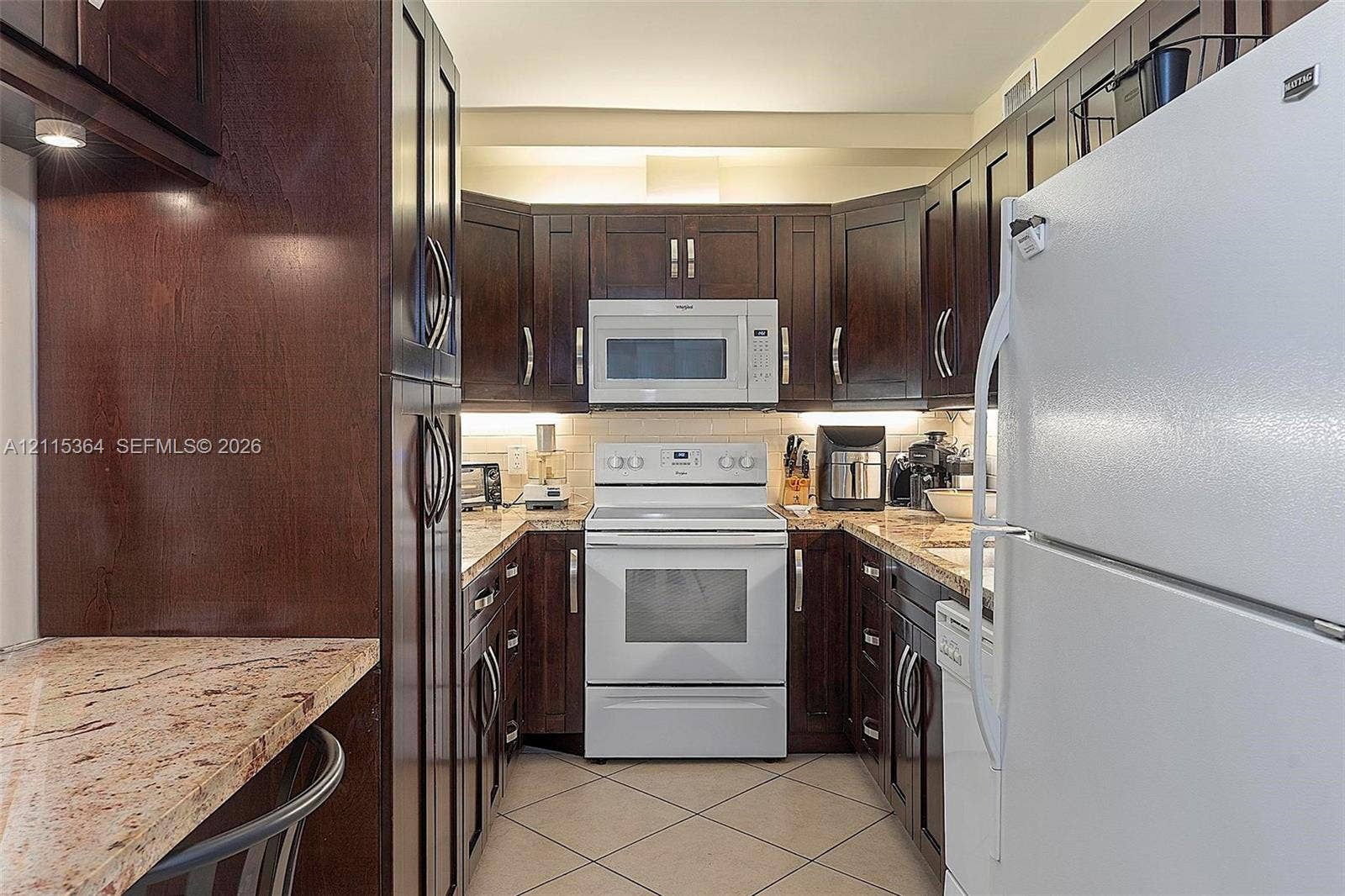 1980 S Ocean Drive, #20A, Hallandale Beach, Hallandale Beach, FL 33009 Dark-stained wood cabinetry, stone countertops, under-cabinet lighting, and white appliances including an electric range and microwave