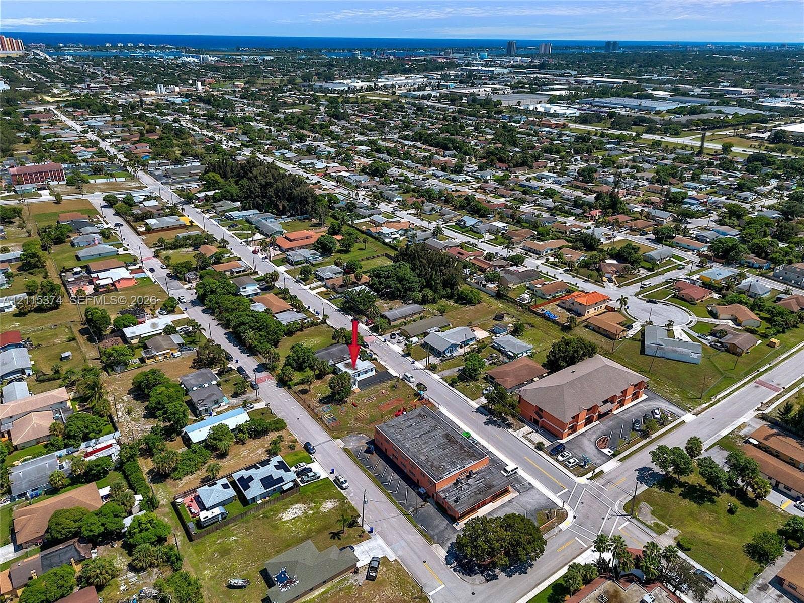 Aerial perspective featuring a single-story residential property with a flat roofline situated on a corner lot, characterized by expansive grounds and mature landscaping