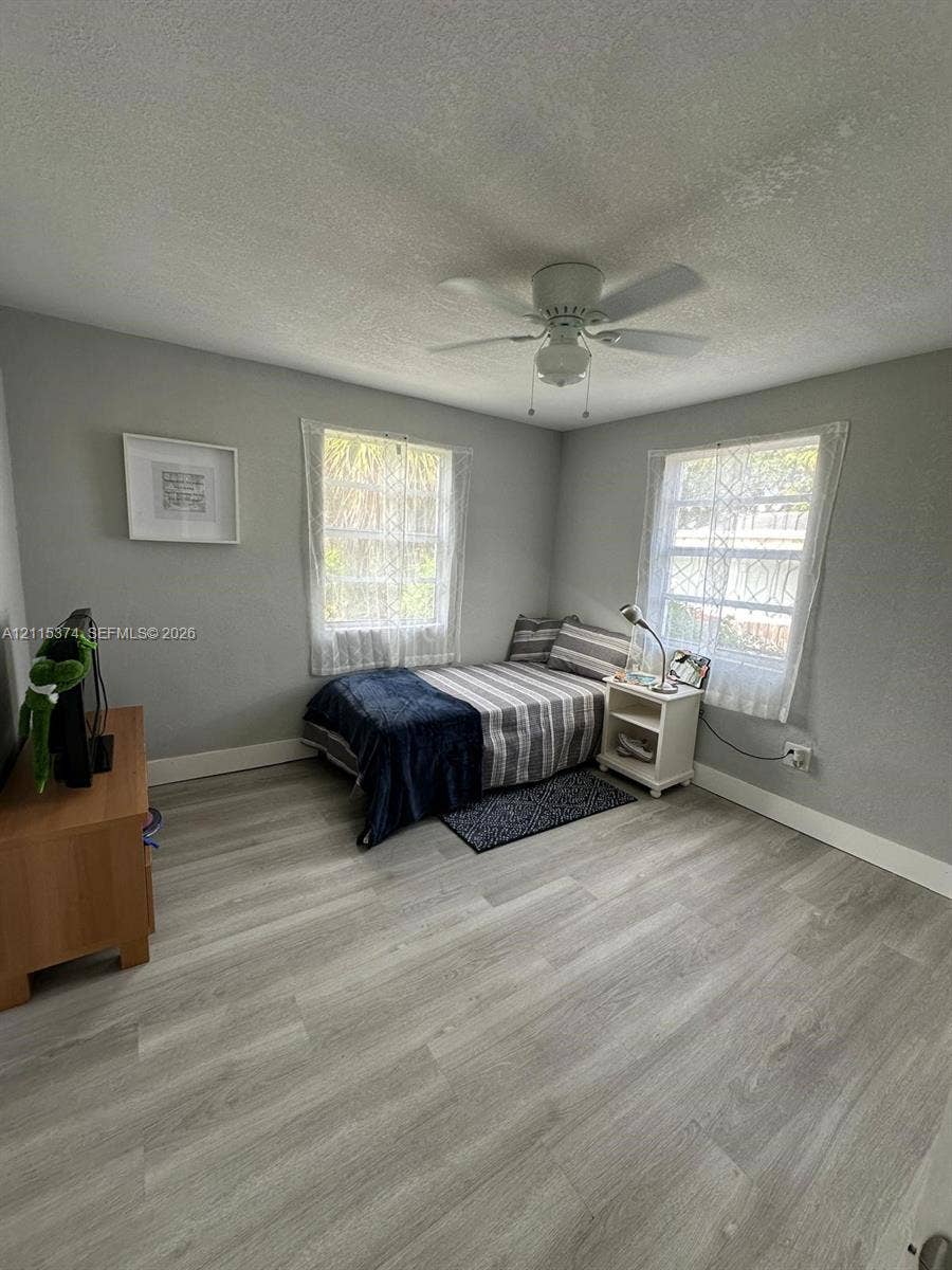 Room featuring neutral wall paint, wood-finish flooring, dual windows, and a ceiling-mounted fan