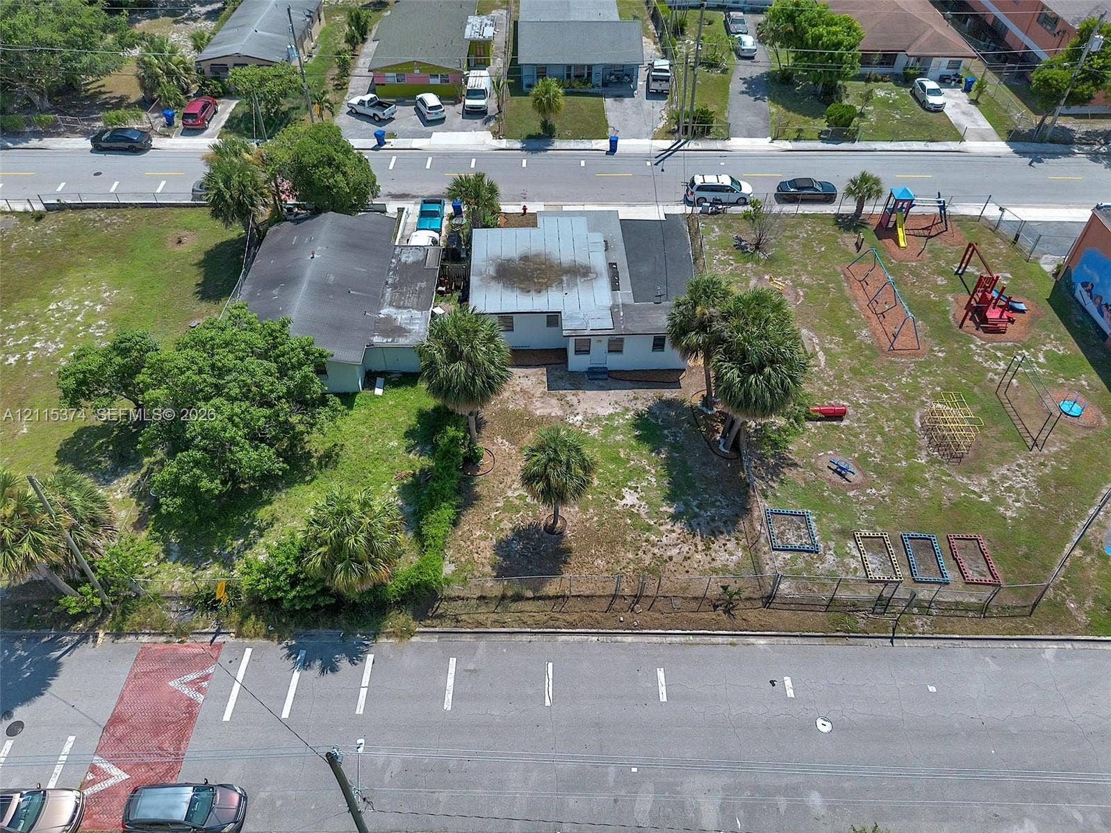 Single-story residence featuring a flat roof and sprawling lot with mature palm trees and established landscaping