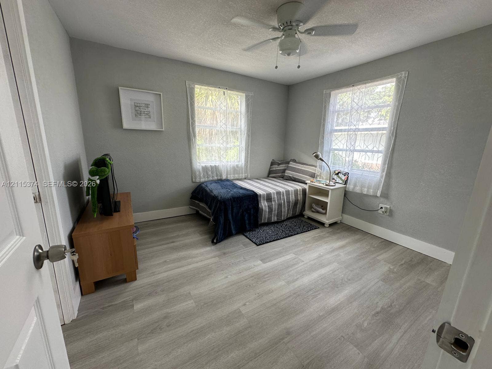 Neutral-toned interior featuring wood-finish flooring, two dual-pane windows, and a central ceiling fan with an integrated light fixture
