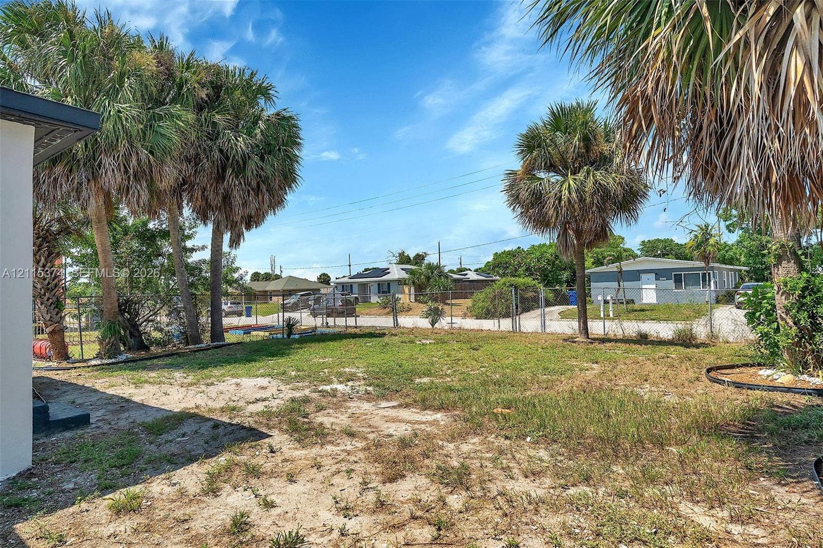 Open backyard area featuring mature palm trees, perimeter chain-link fencing, and sandy turf