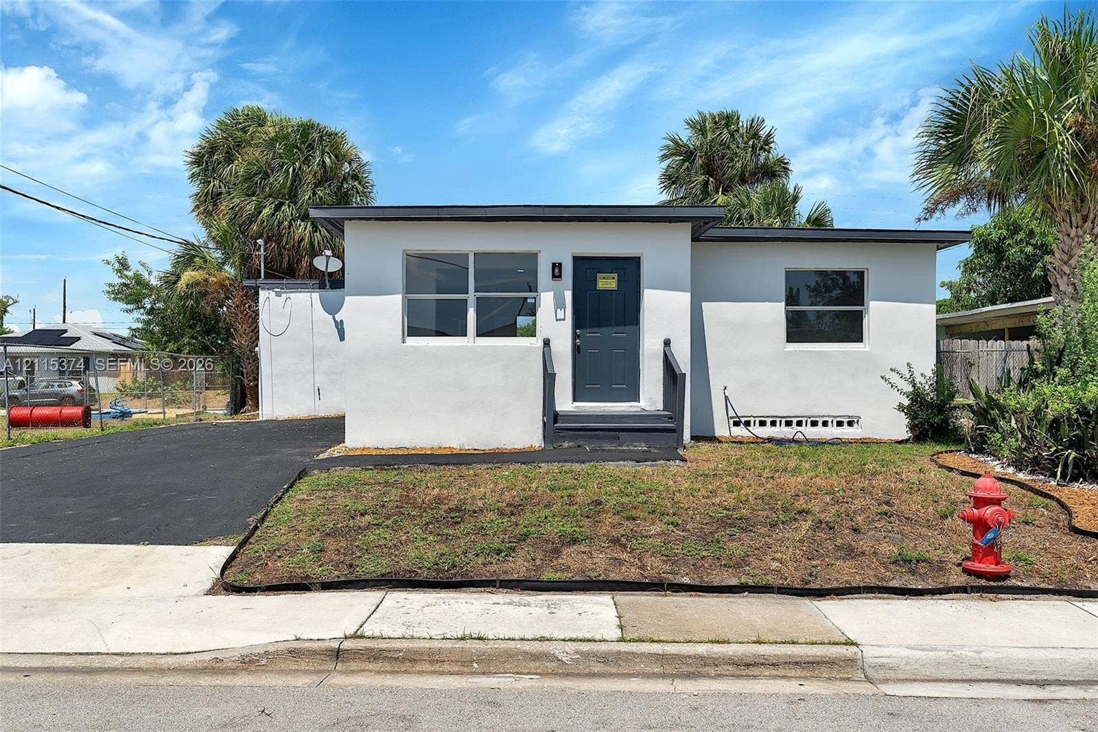 Single-story exterior featuring white stucco siding, a flat roofline, an asphalt driveway, and a dark-toned entry door with matching stairs