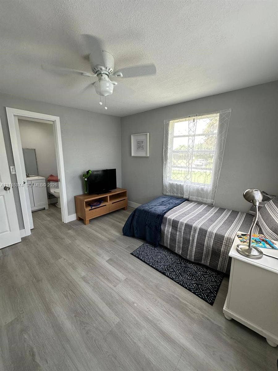 Interior space featuring wood-finish flooring, a neutral color palette, and a multi-blade ceiling fan with a center light fixture