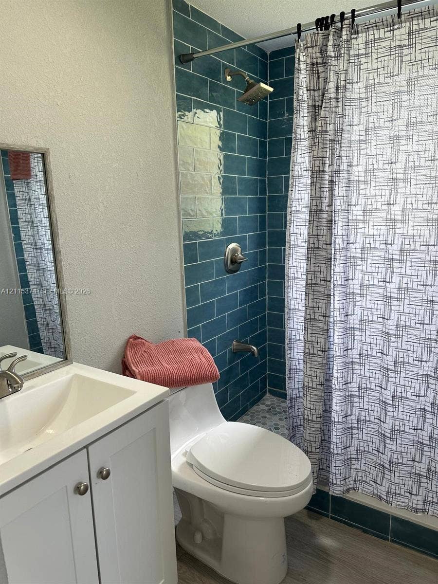 Bathroom featuring a white vanity cabinet, rectangular sink, framed mirror, and a shower surround finished with blue subway tile