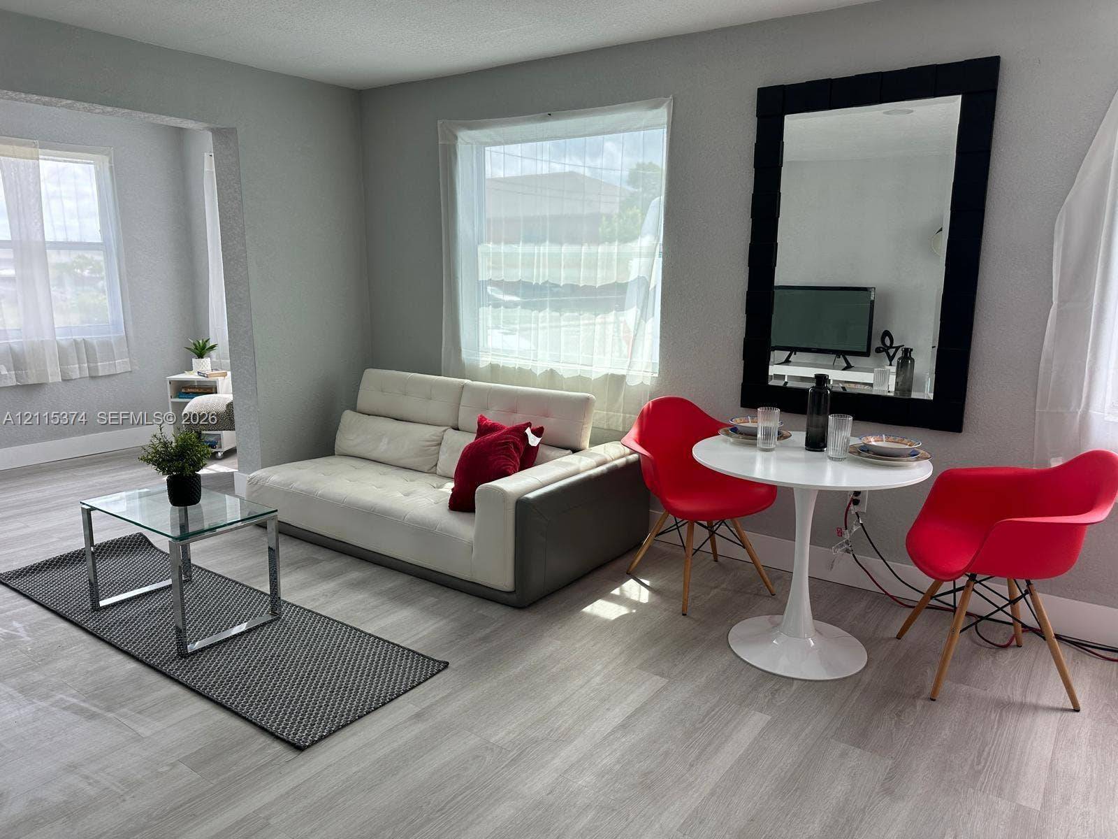 Neutral-toned wood-finish flooring, large picture window, and wall-mounted oversized rectangular mirror with black frame