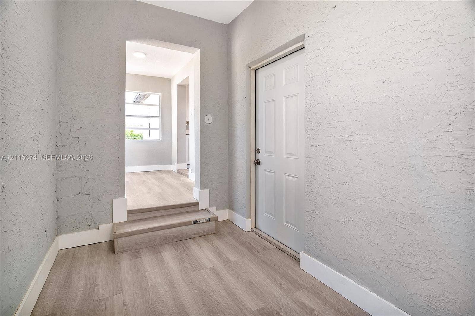 Entryway featuring light-toned wood-finish flooring, a six-panel door, and textured gray wall finishes