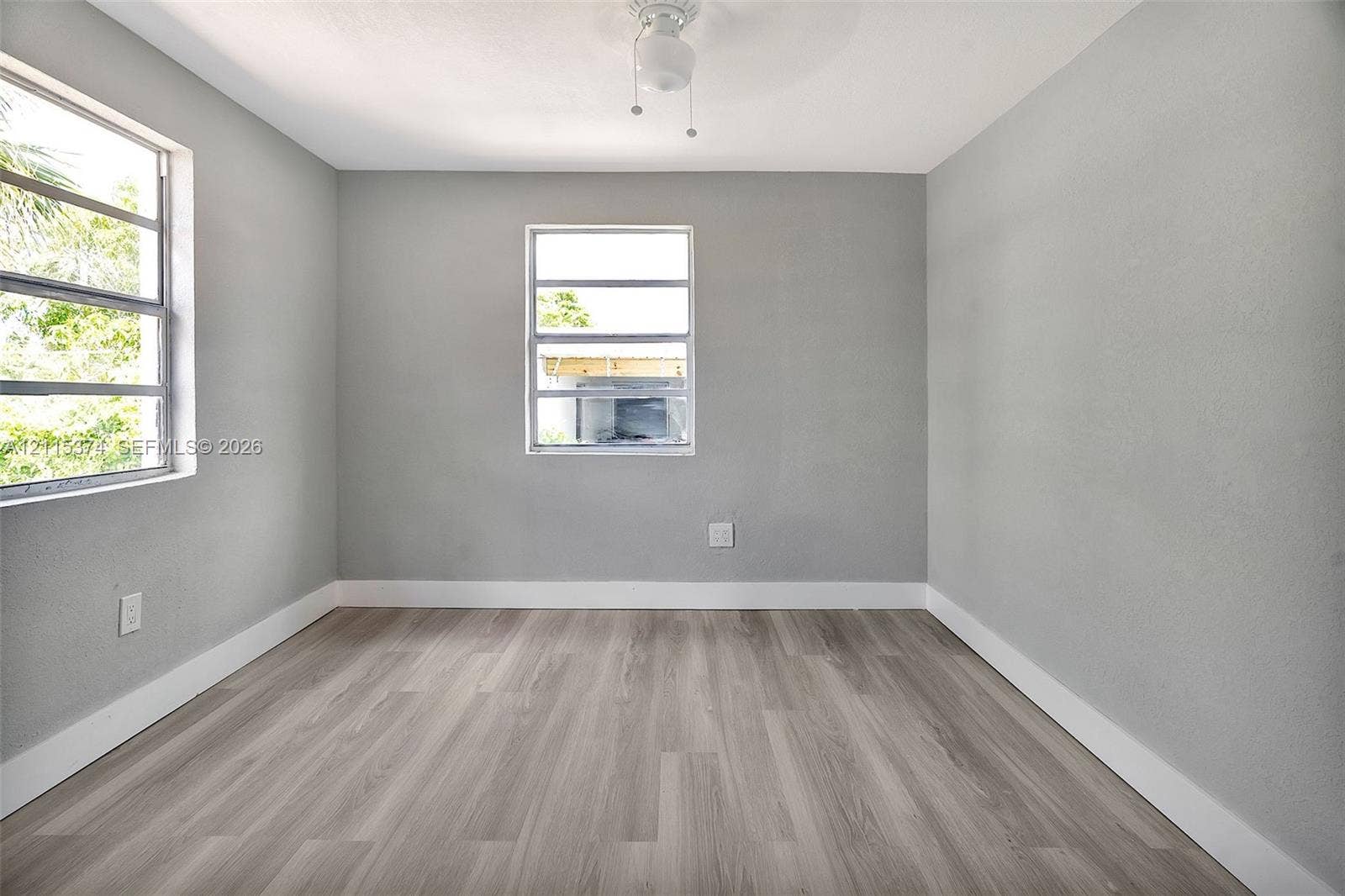 Neutral-toned interior space featuring wood-finish flooring, two horizontal sliding windows, and a central ceiling fan