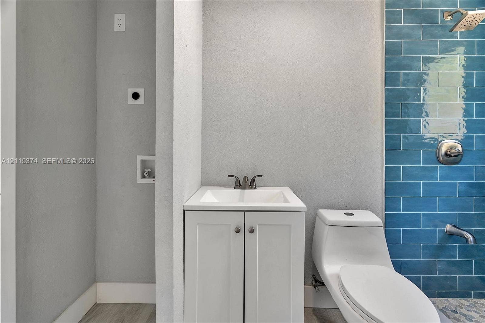White vanity with a rectangular basin, chrome faucet, one-piece dual-flush toilet, and blue subway tile shower surround with a rainfall showerhead