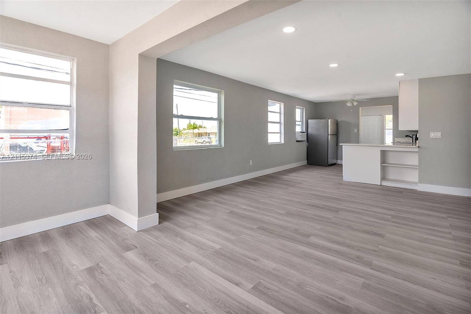 Open-concept interior featuring wood-finish flooring, recessed lighting, white cabinetry, and multiple windows