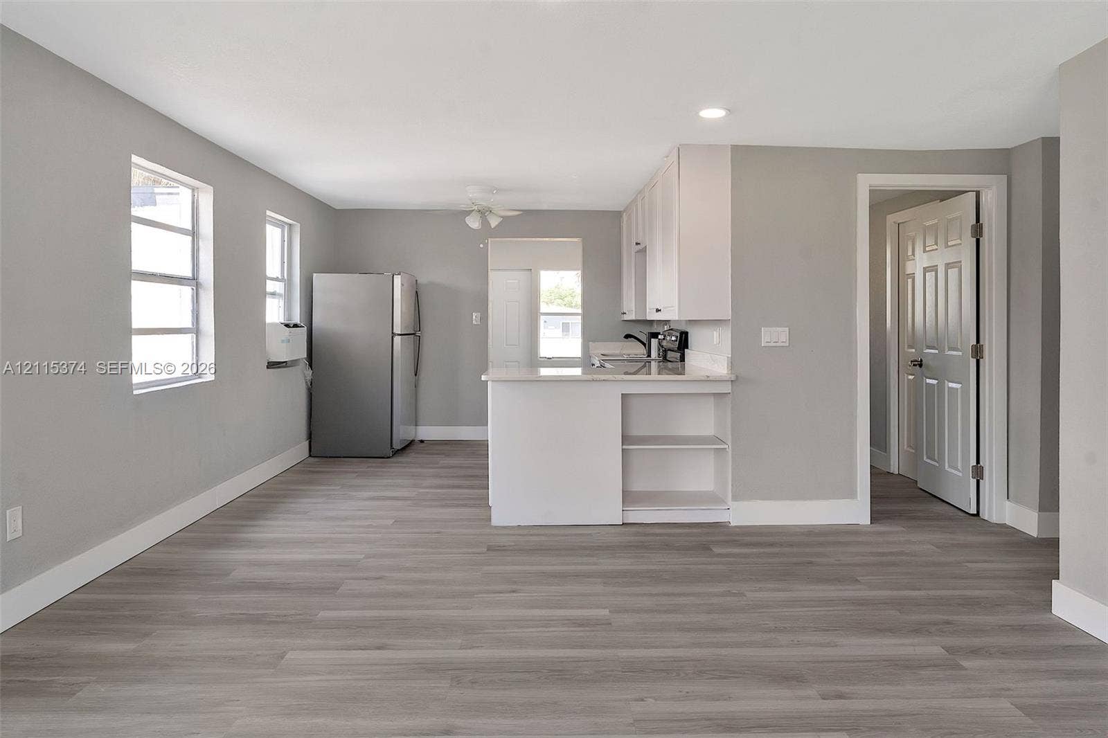 Kitchen featuring wood-finish flooring, white cabinetry, a peninsula with integrated shelving, and stainless steel refrigerator