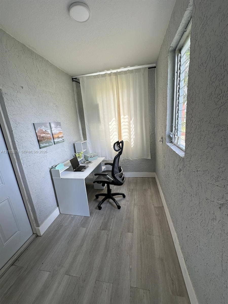 Room featuring wood-finish flooring, textured wall finishes, and a window with louvered glass panes