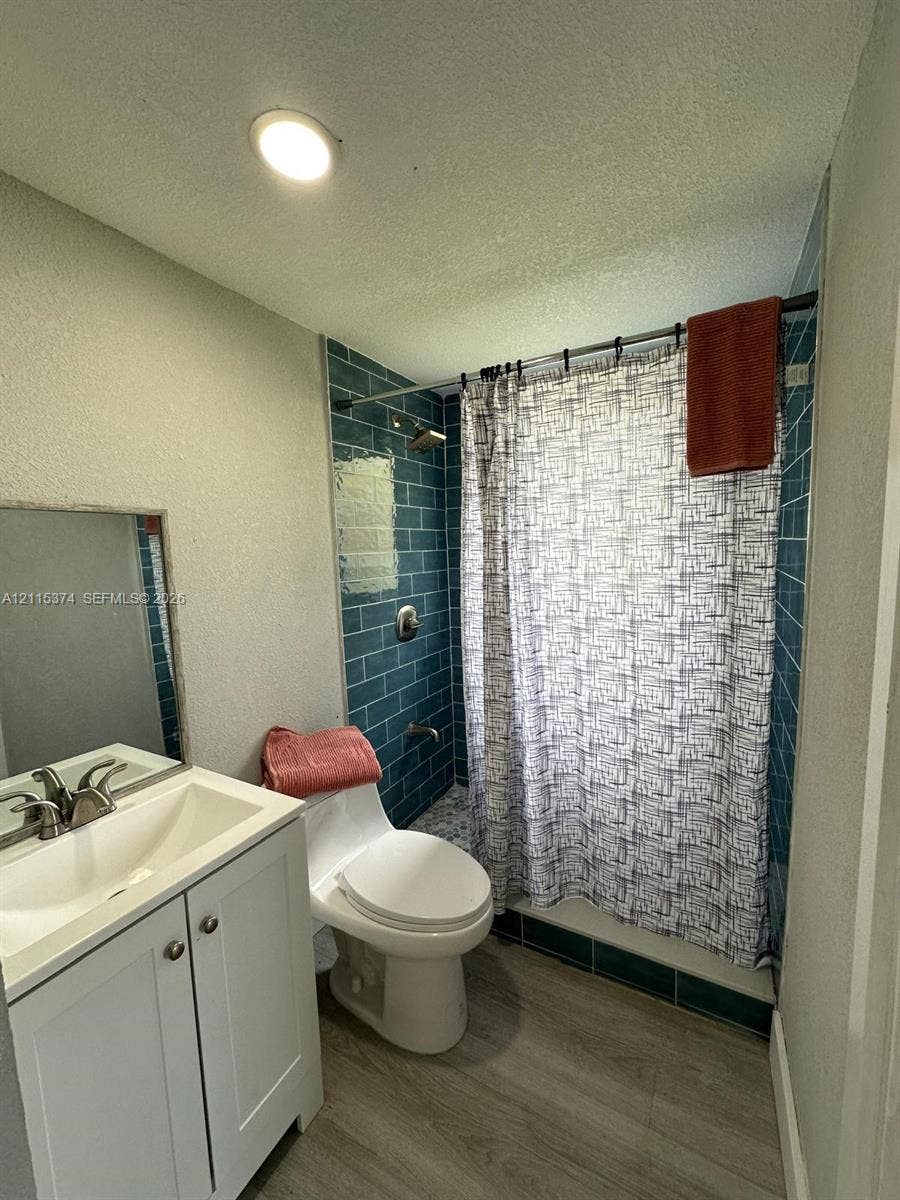 Bathroom featuring a white vanity cabinet with an integrated basin, brushed nickel faucet, blue subway tile shower surround, and wood-finish flooring