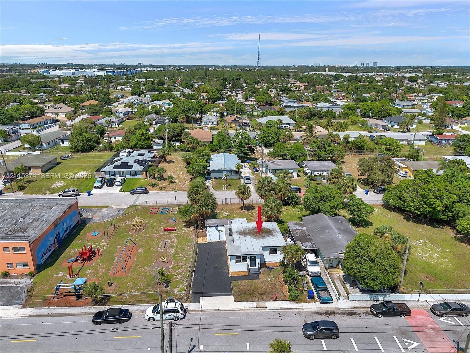 Aerial perspective featuring a single-story structure with a metal roof, asphalt driveway, and peripheral landscaping