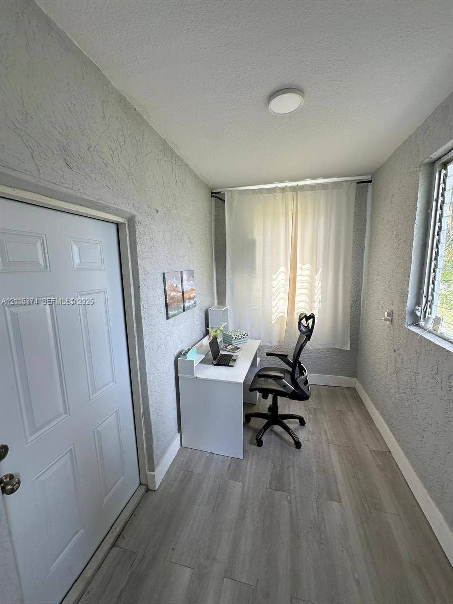 Neutral-toned wood-finish flooring, textured wall finishes, solid-core interior door with metallic hardware, and flush-mount ceiling lighting