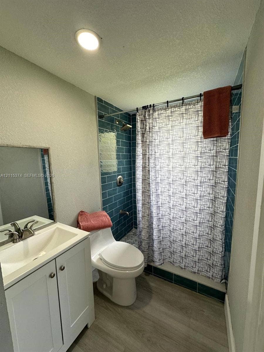 Bathroom featuring wood-finish flooring, white vanity with integrated sink, chrome-finish faucet, and blue subway-tiled shower surround