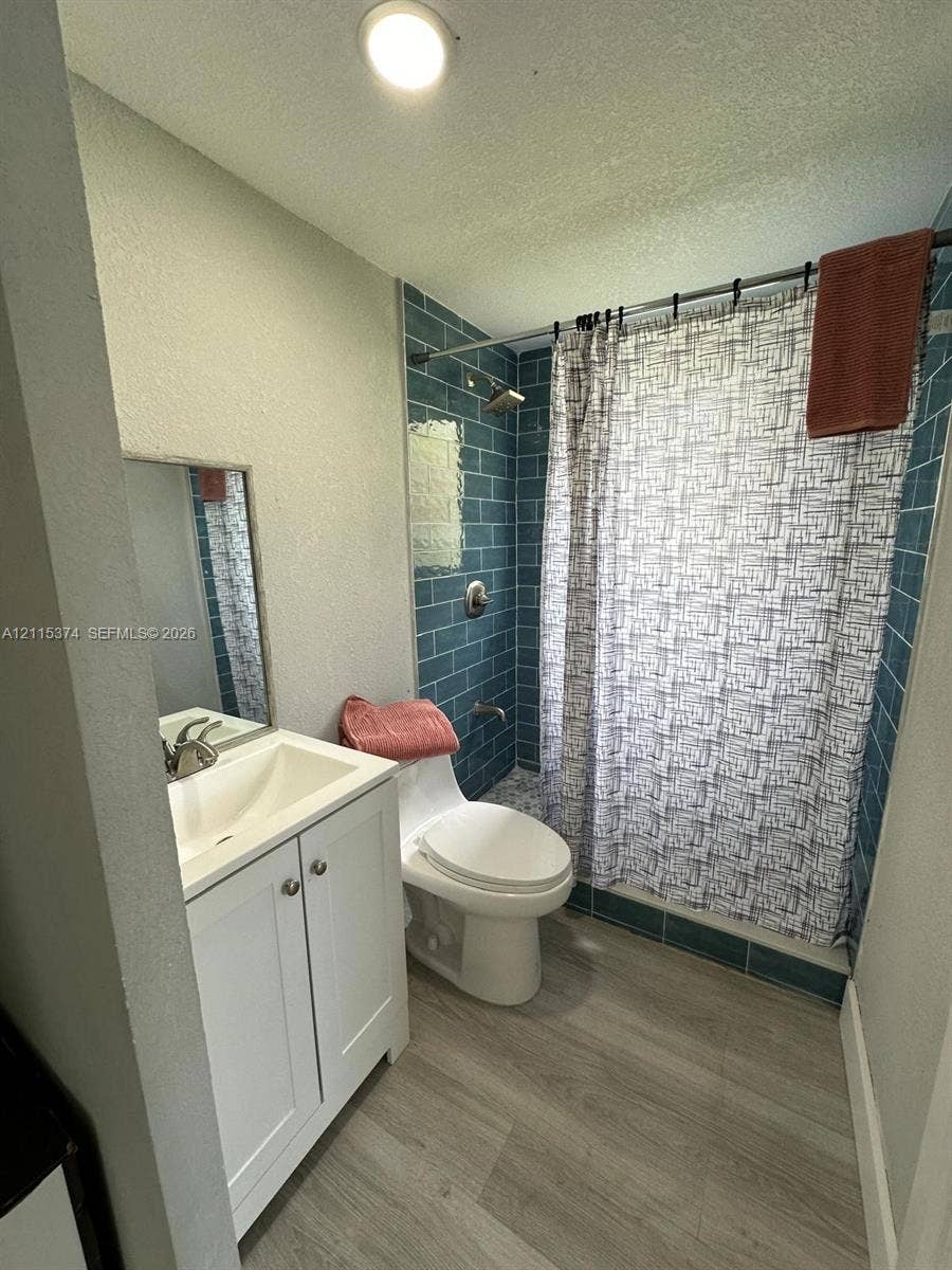 White shaker-style vanity with integrated sink, wood-finish flooring, and shower enclosure featuring blue subway-style tile surrounds