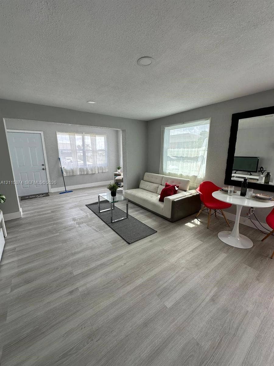 Open-concept room featuring light-toned wood-finish flooring, recessed lighting, and large windows providing natural illumination