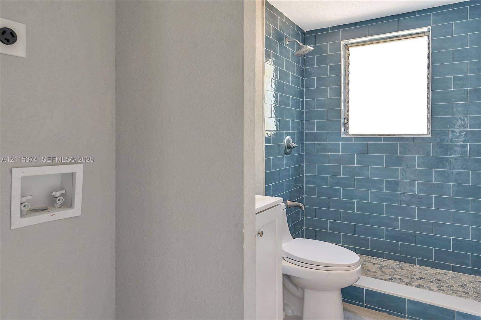 Blue subway tile shower surround, mosaic pebble-style shower floor, built-in water utility connections, and white vanity cabinetry