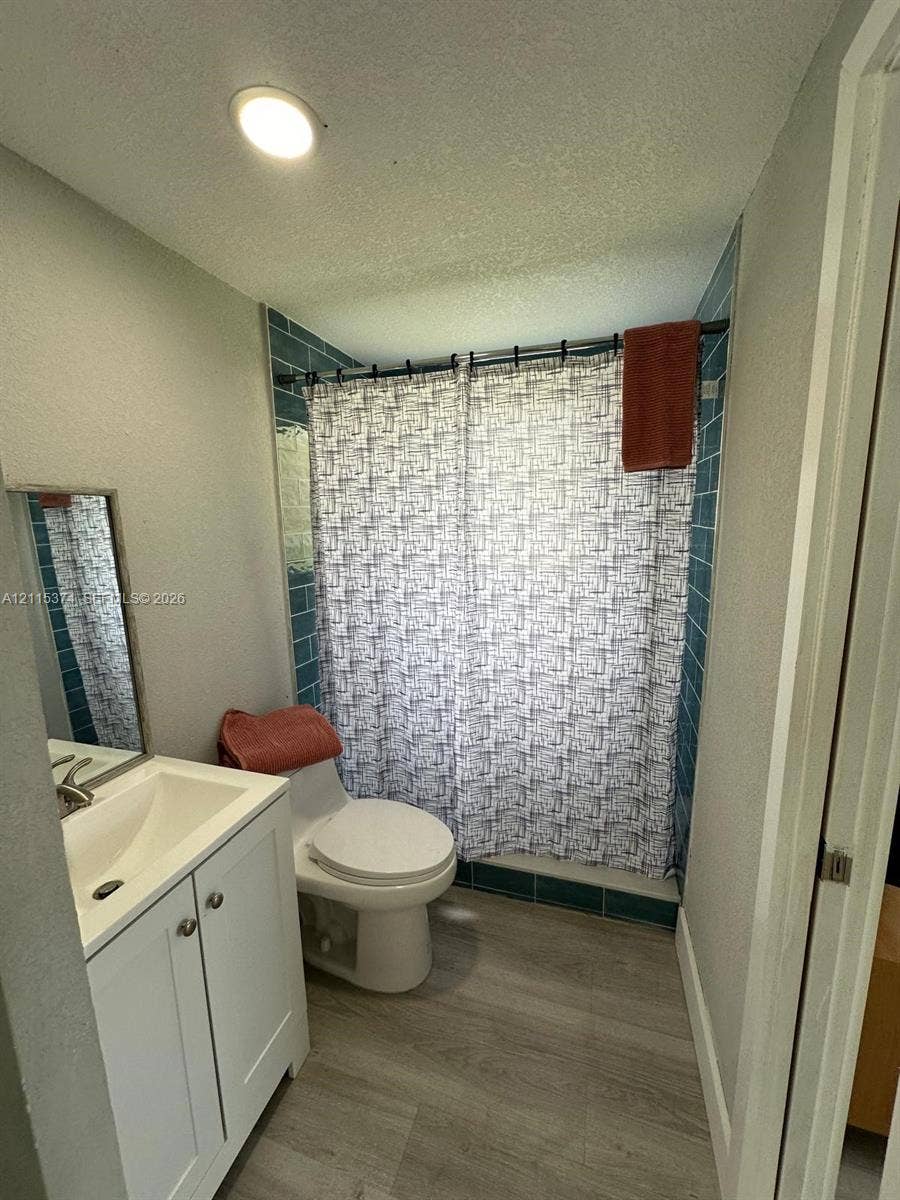 Bathroom featuring wood-finish flooring, a white vanity with an integrated sink, a tiled shower surround, and a recessed ceiling light