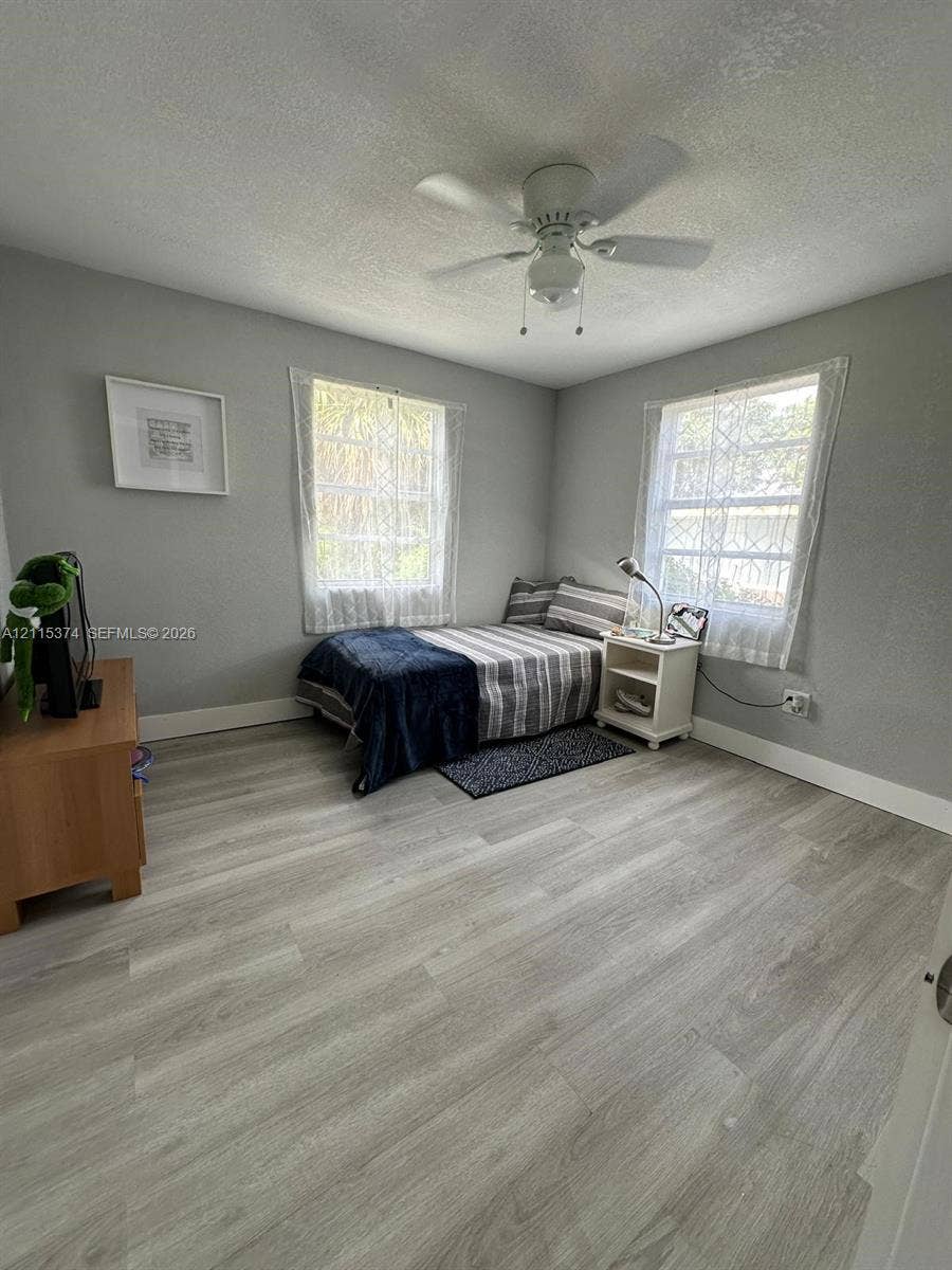 Room featuring wood-finish flooring, two windows with diamond-pattern muntins, and a ceiling-mounted light fixture with a fan