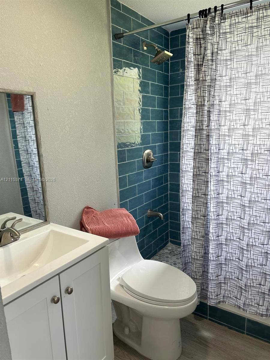 Bathroom featuring a white vanity cabinet with an integrated basin, wall-mounted mirror, ceramic subway tile shower surround in a blue finish, and wood-finish flooring