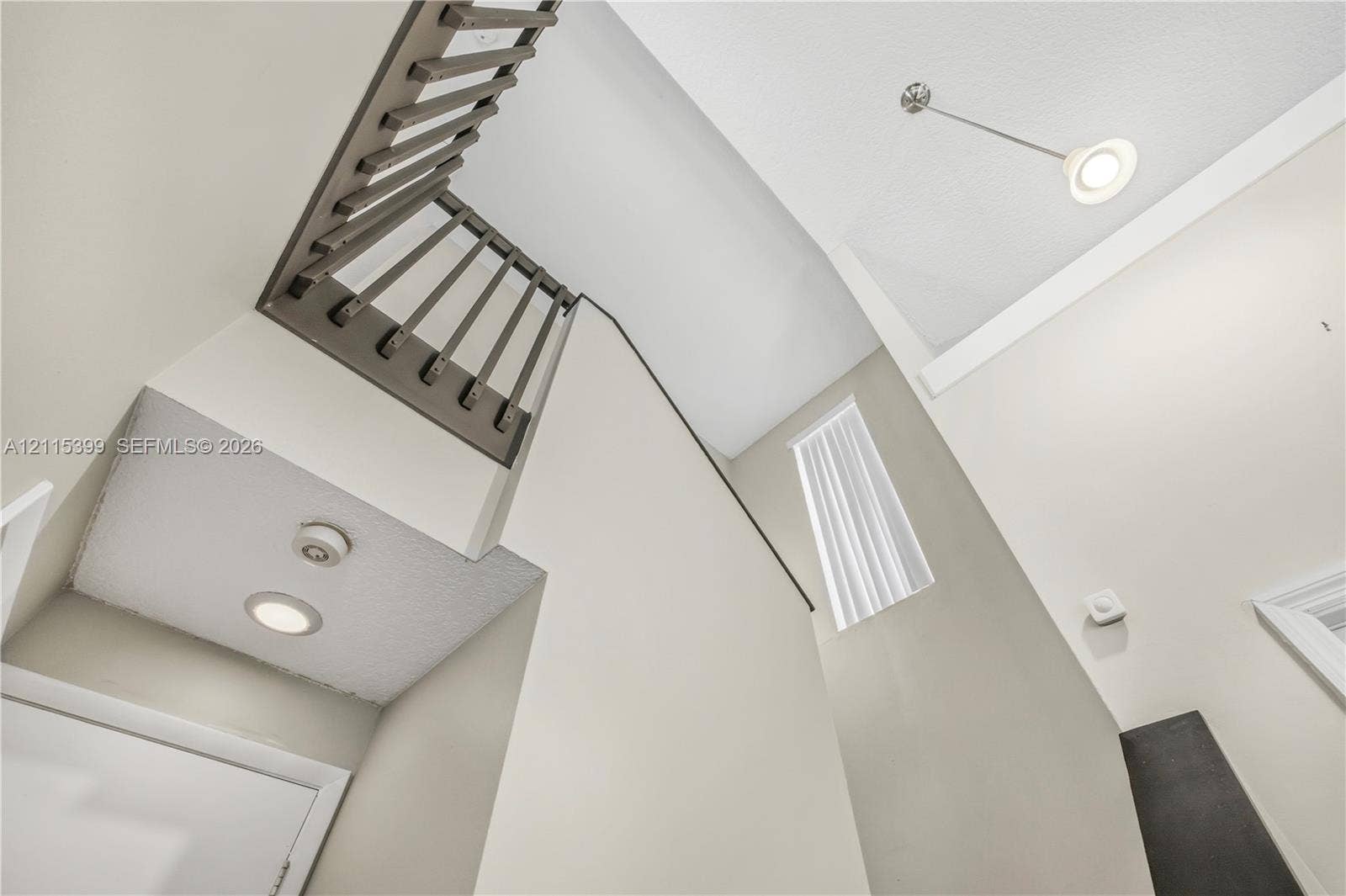 High-ceiling entryway featuring a staircase with dark-finished railings, vertical rectangular window, recessed lighting, and a pendant fixture