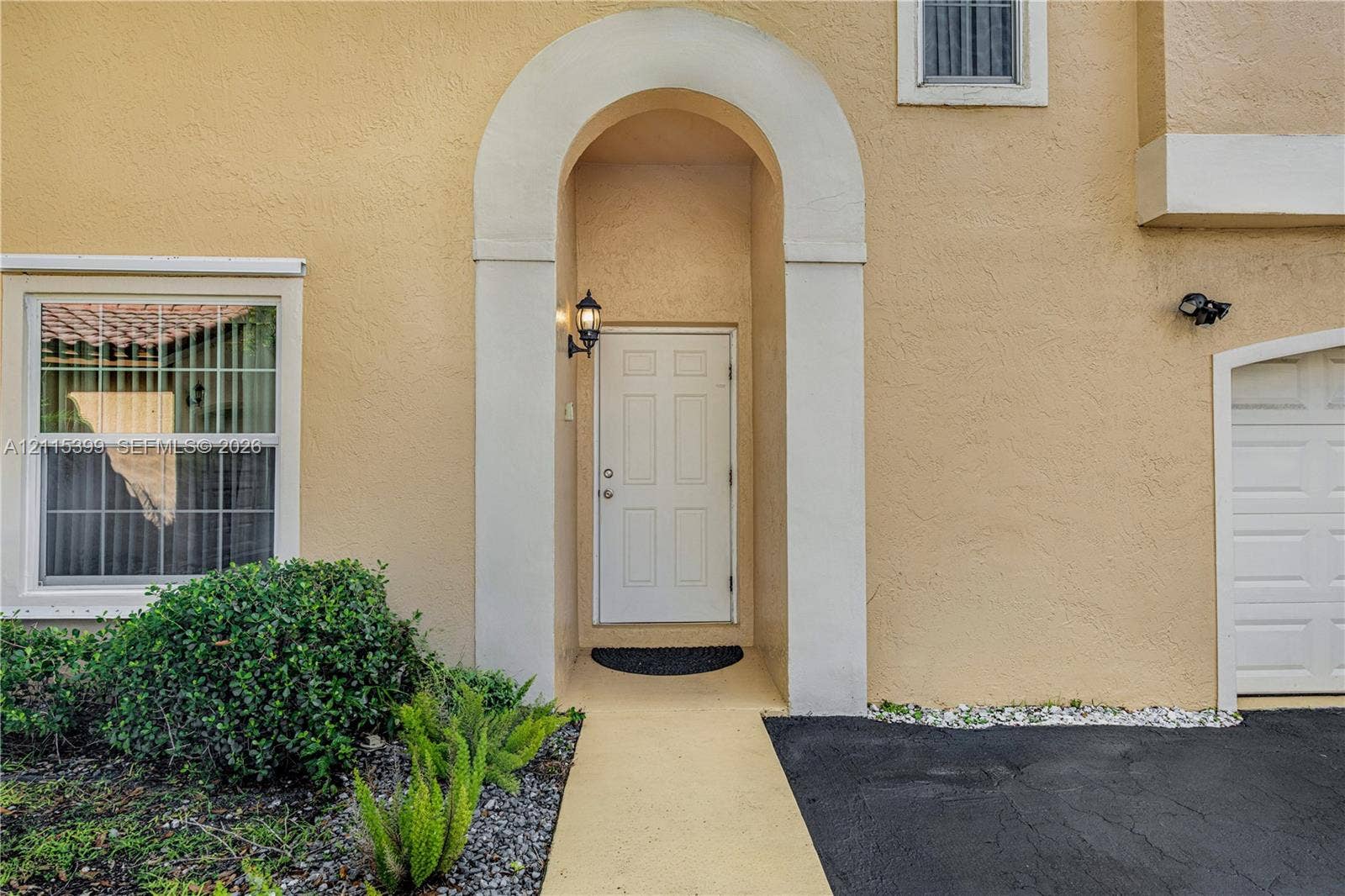 Stucco exterior featuring a recessed entryway with a rounded arched surround, a six-panel front door, and a single-car garage with a sectional door