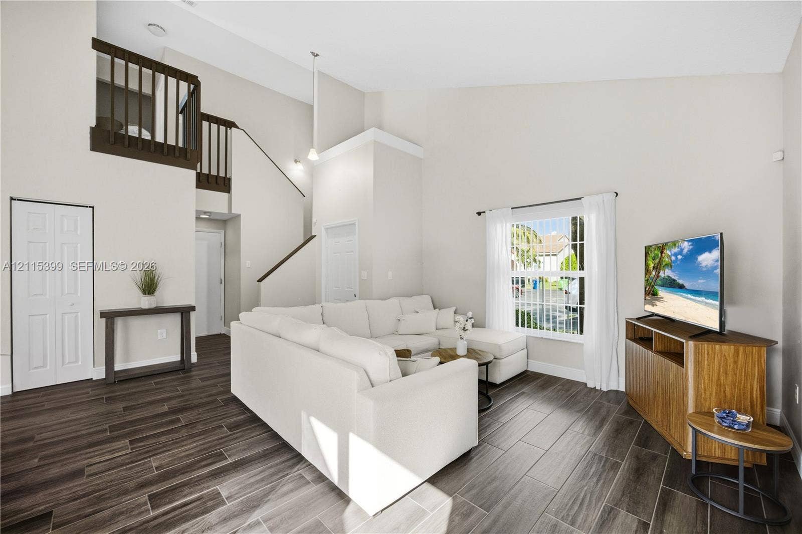 Living area featuring vaulted ceilings, wood-finish tile flooring, a mezzanine balcony with dark-finish railing, and a window with natural light