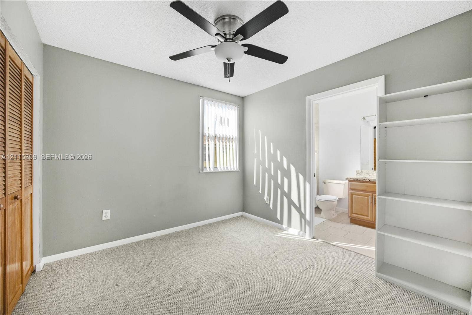 Neutral interior space featuring carpeted flooring, a ceiling fan, a window with vertical blinds, and a built-in wooden closet