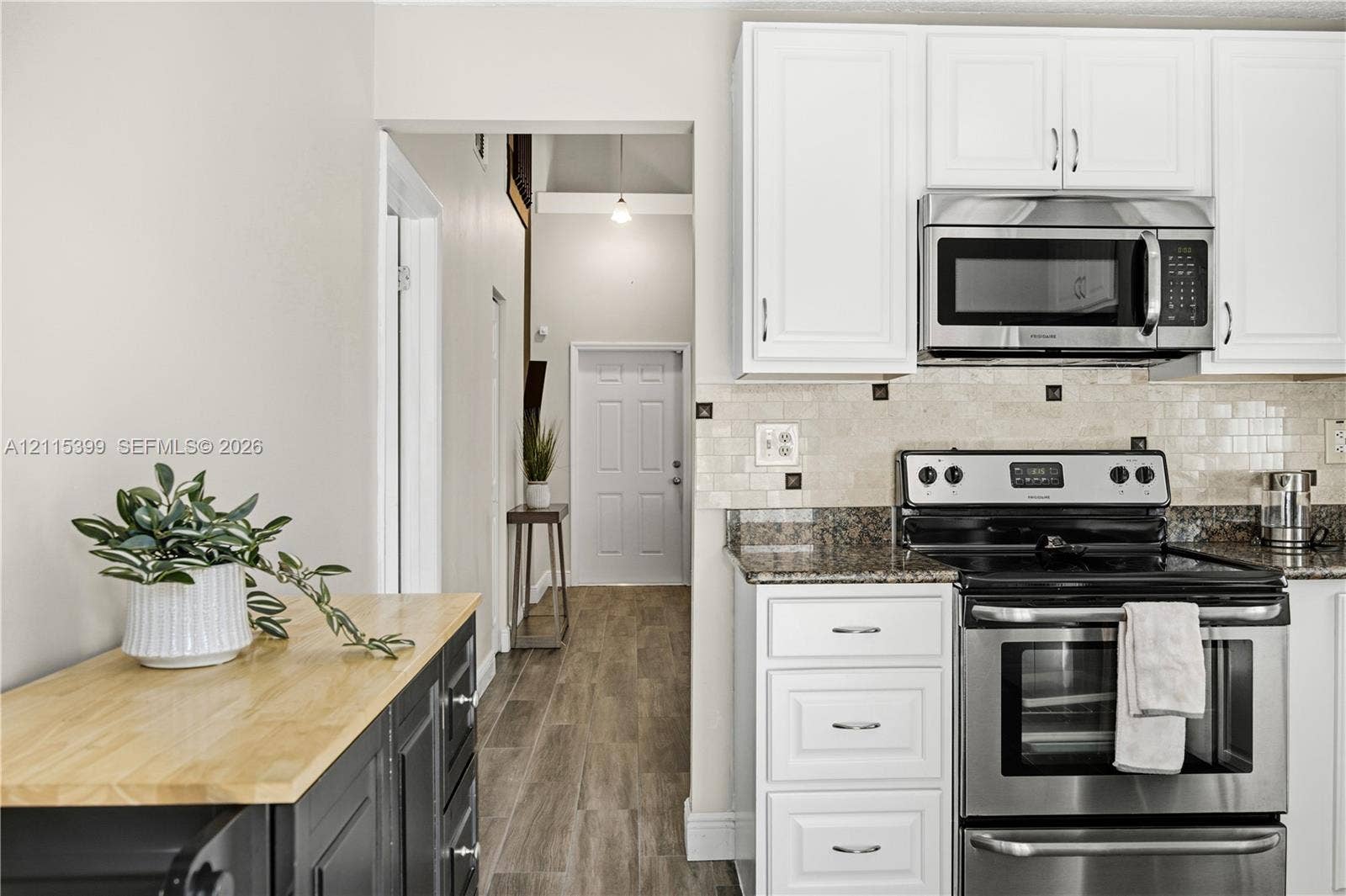 Kitchen featuring white cabinetry, stainless steel appliances, stone-finish countertops, tiled backsplash, and wood-finish flooring