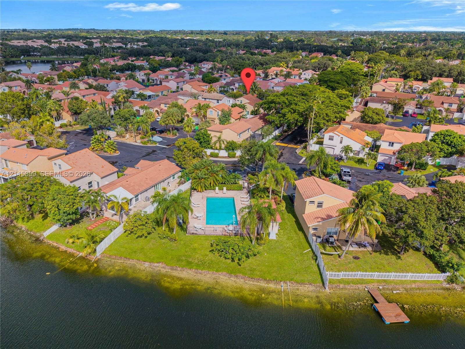 Aerial perspective of a waterfront property featuring a fenced swimming pool, private boat dock, green space, and mature landscaping
