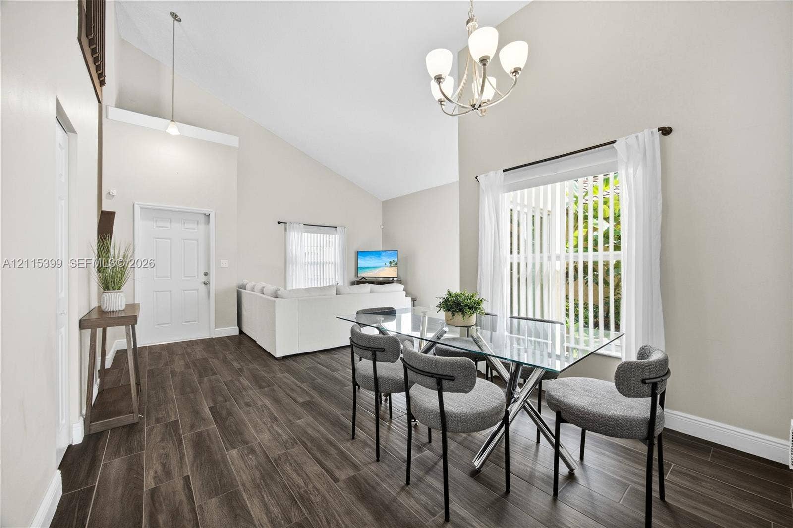 Vaulted ceilings, wood-finish flooring, multi-arm chandelier, and sliding glass door with vertical blinds