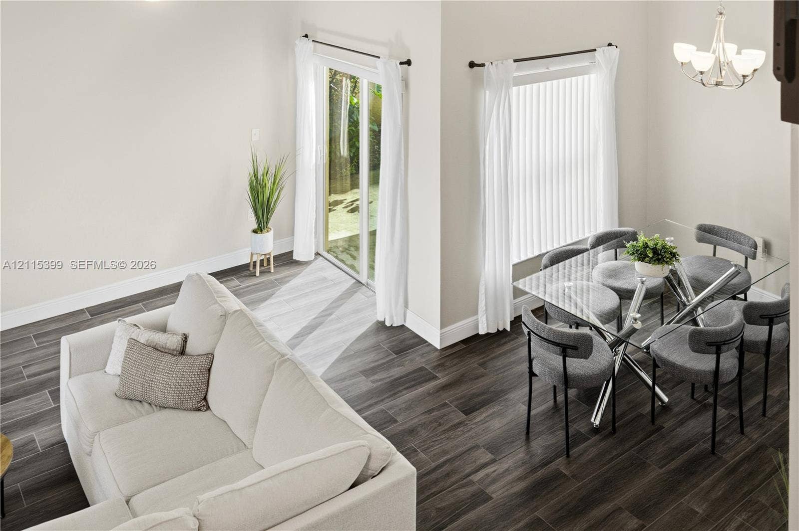 Open-concept interior featuring wood-finish tile flooring, vaulted ceilings, a sliding glass door, and a five-arm multi-light chandelier