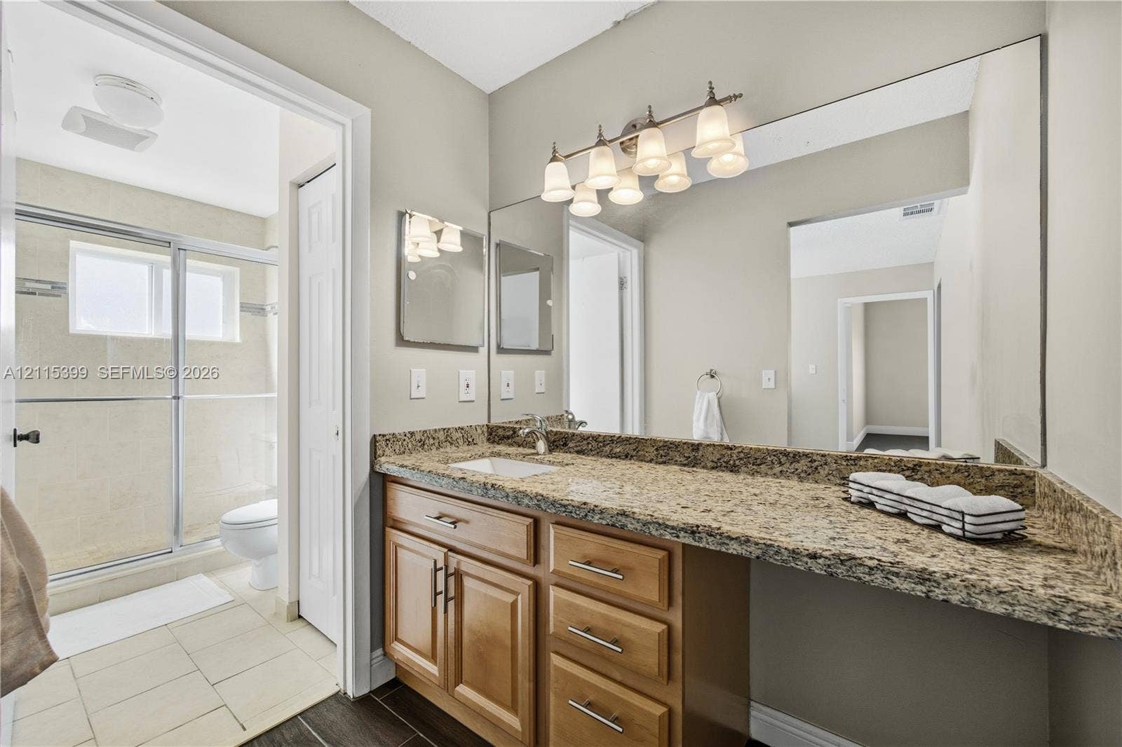 Bathroom featuring a vanity with stone-finish countertop, undermount sink, shaker-style wood cabinetry, full-width mirror, and a walk-in shower with sliding glass doors