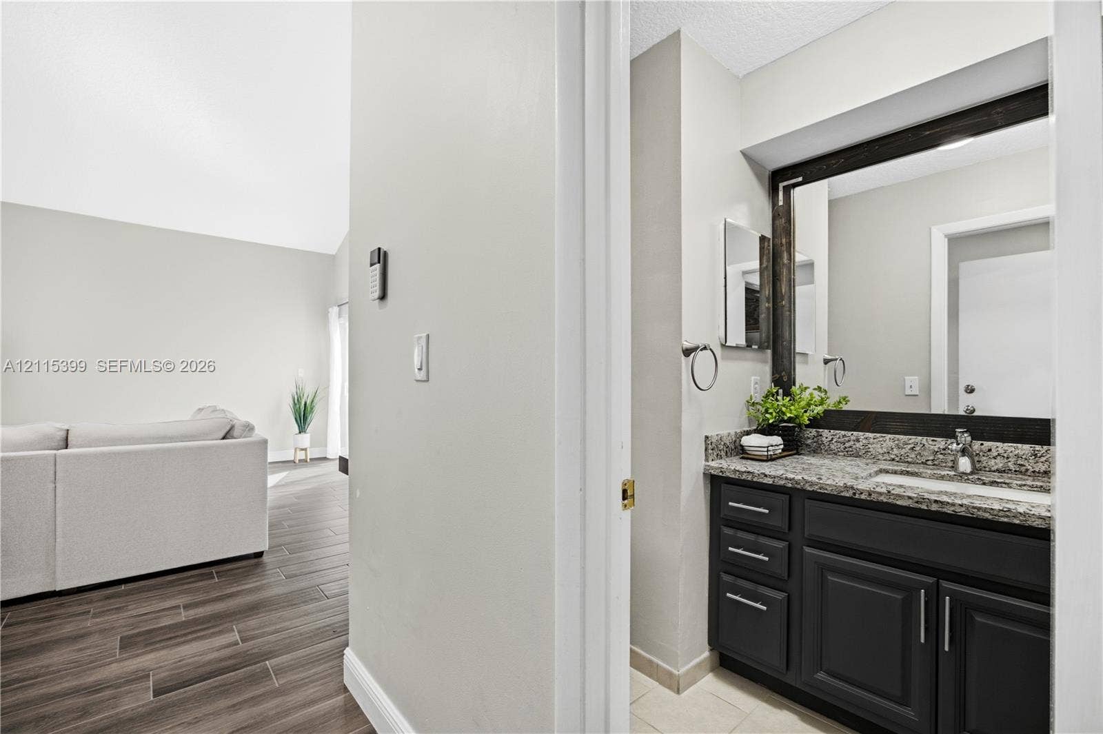 Bathroom featuring a dark-finish vanity with stone-patterned countertop, an undermount sink, and a large framed mirror