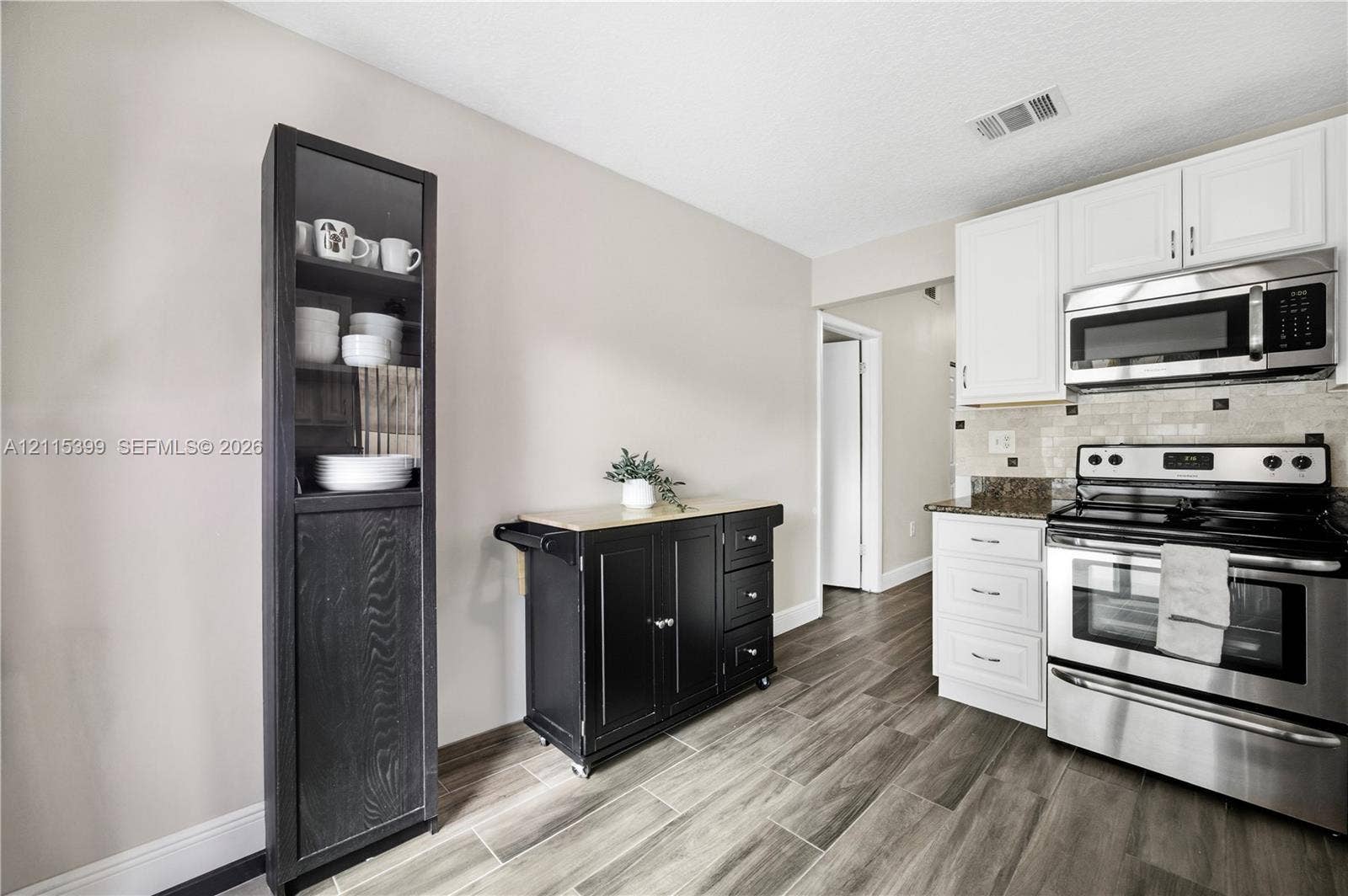 Kitchen featuring white cabinetry, stainless steel appliances, integrated over-the-range microwave, stone-finish countertops, and wood-finish flooring