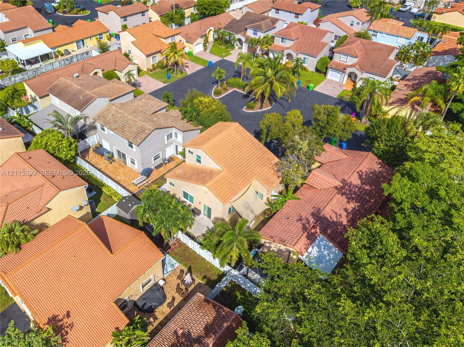 Aerial perspective of a multi-level residence featuring a clay tile roof, stucco exterior, fenced perimeter, and mature landscaping