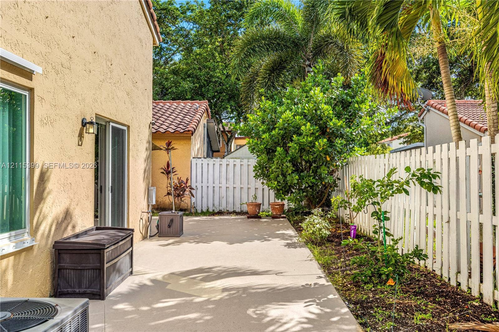 Stucco exterior wall with integrated wall-mounted light fixture, concrete patio, and white vertical picket fencing