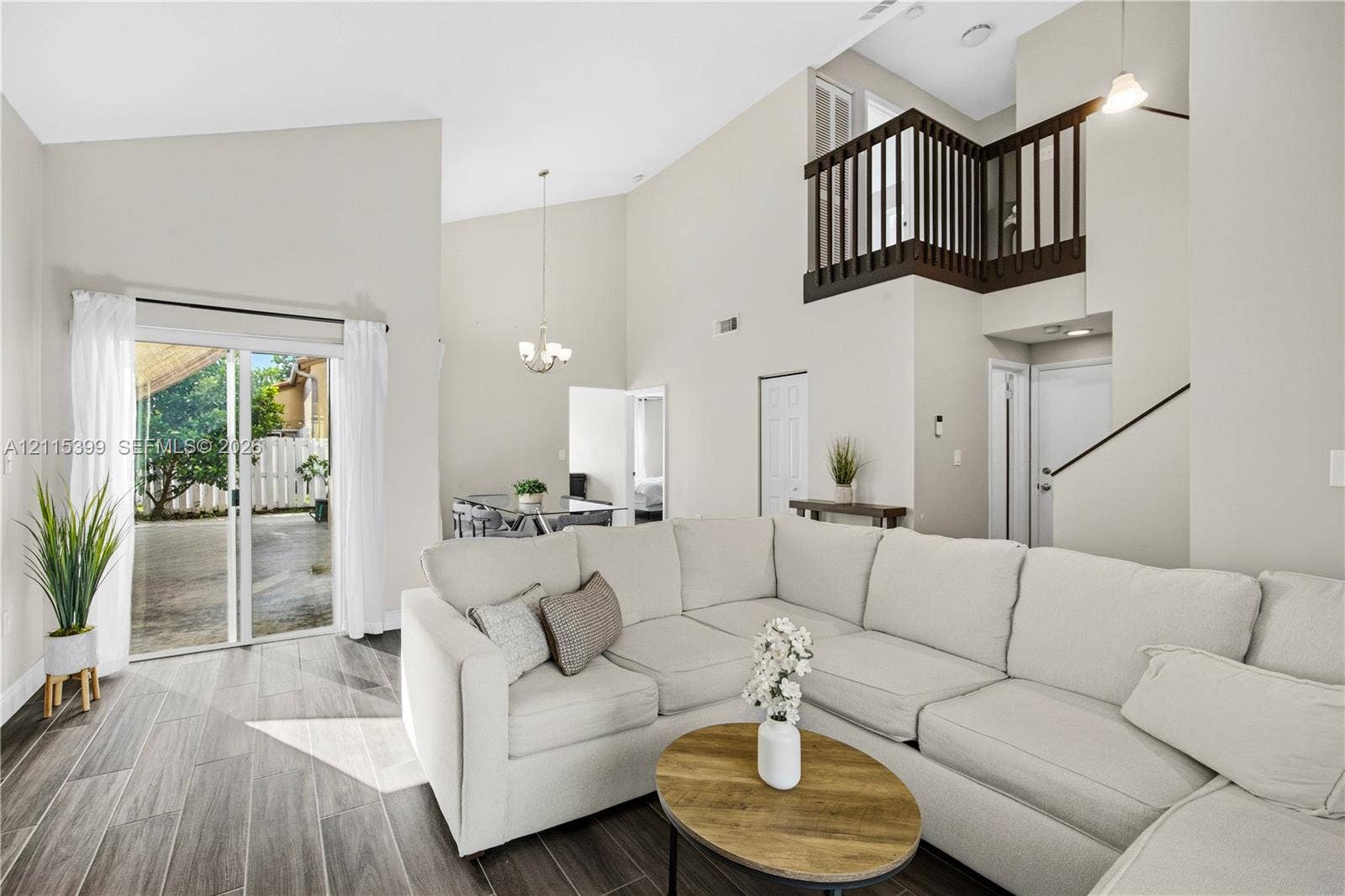 Vaulted ceiling featuring a neutral color palette, wood-finish flooring, sliding glass door access to the exterior, and a mezzanine with a dark wood-finish railing