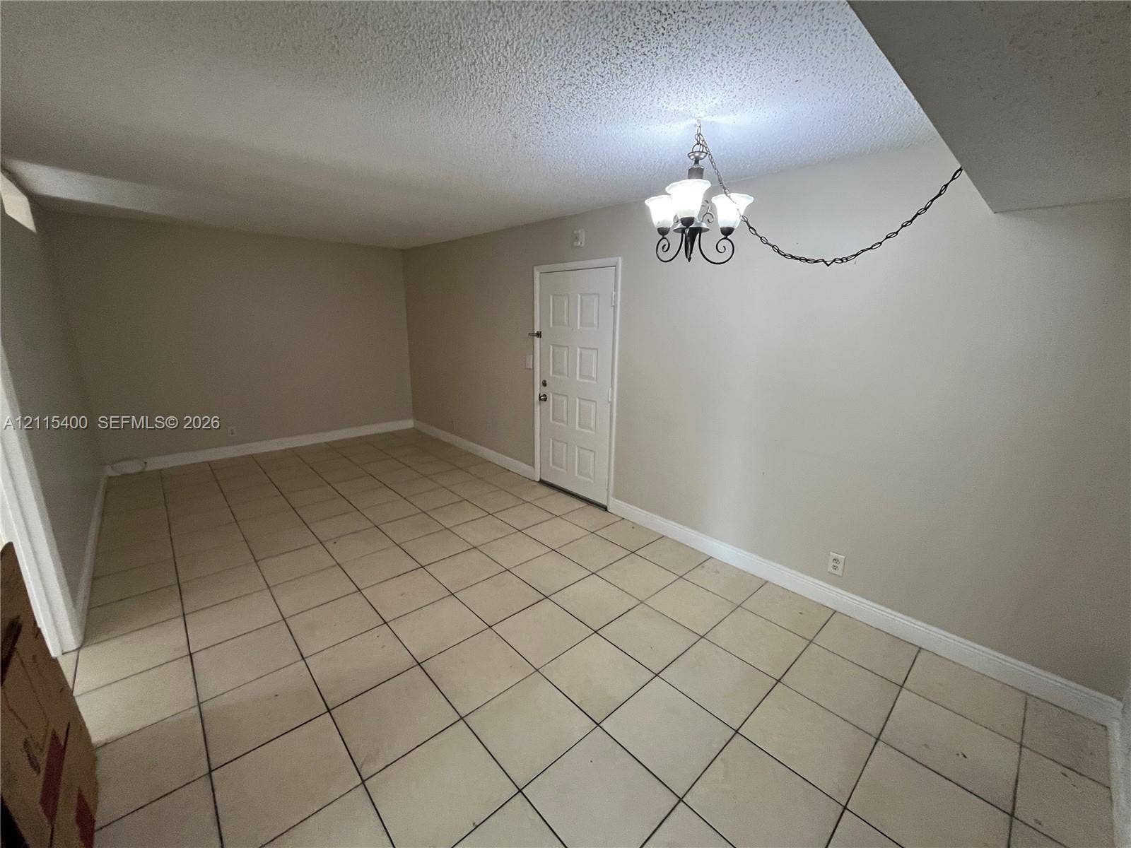 Interior space featuring neutral wall paint, ceramic tile flooring, a multi-panel door, and a suspended multi-light chandelier