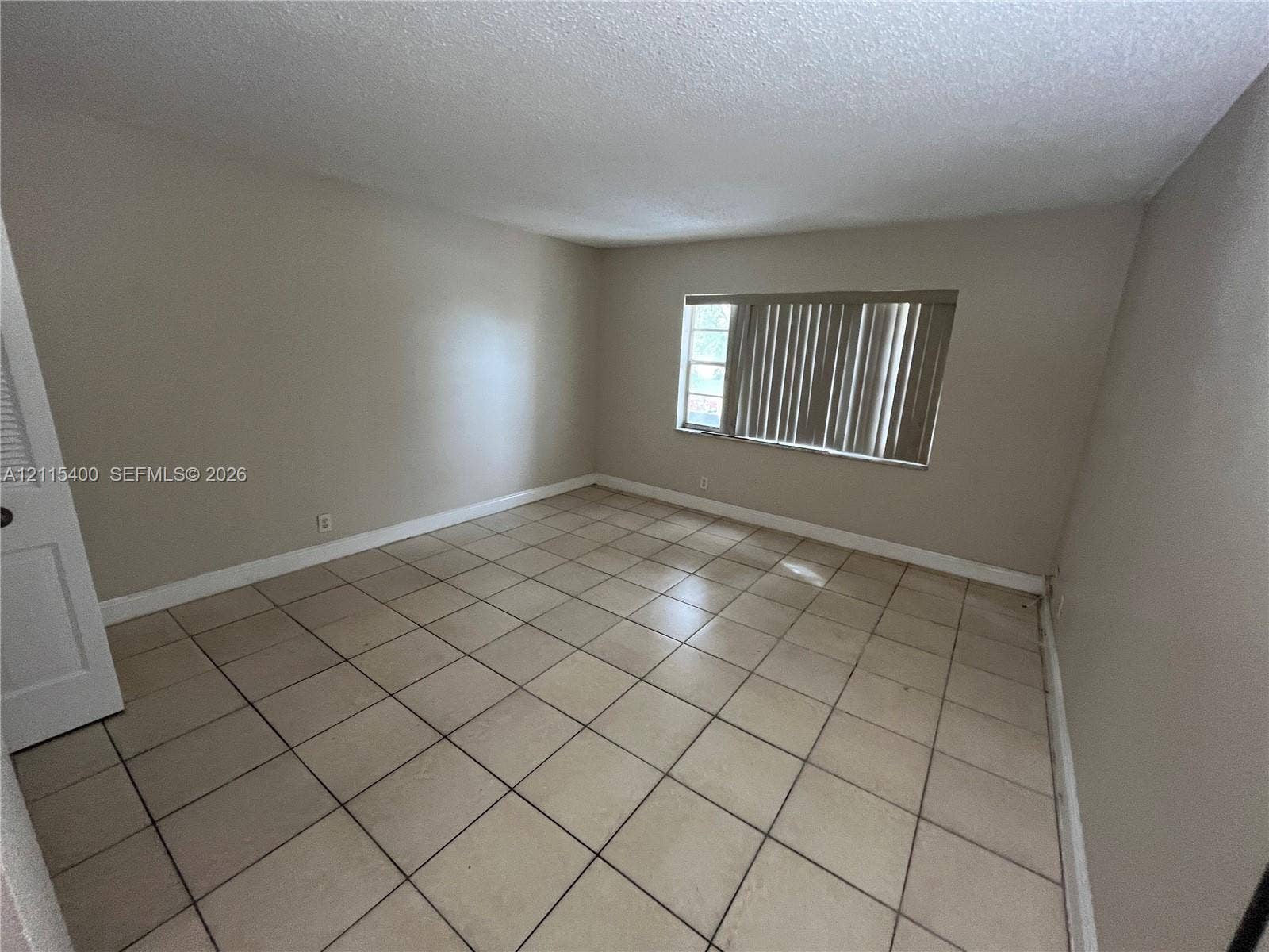 Neutral interior room featuring tile flooring, smooth-finish walls, and a window with vertical blinds