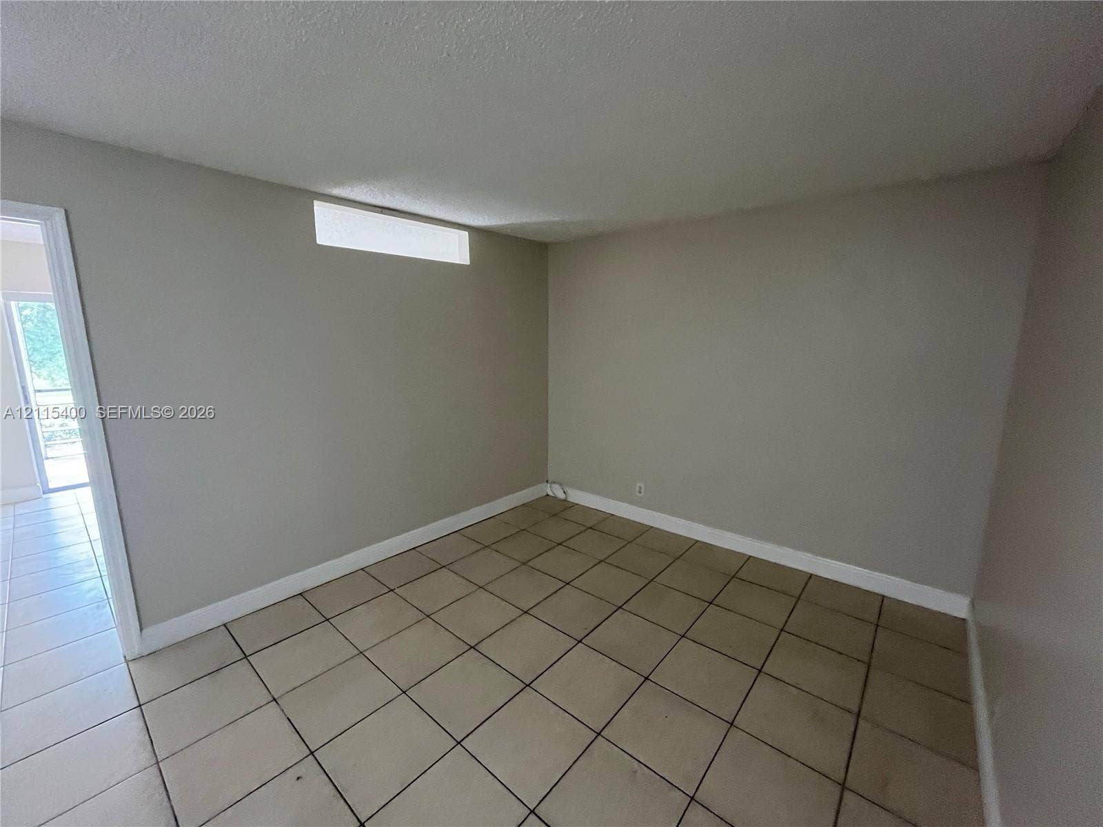 Neutral-toned interior space featuring ceramic tile flooring, a high-set horizontal window, and a door frame leading to a separate area