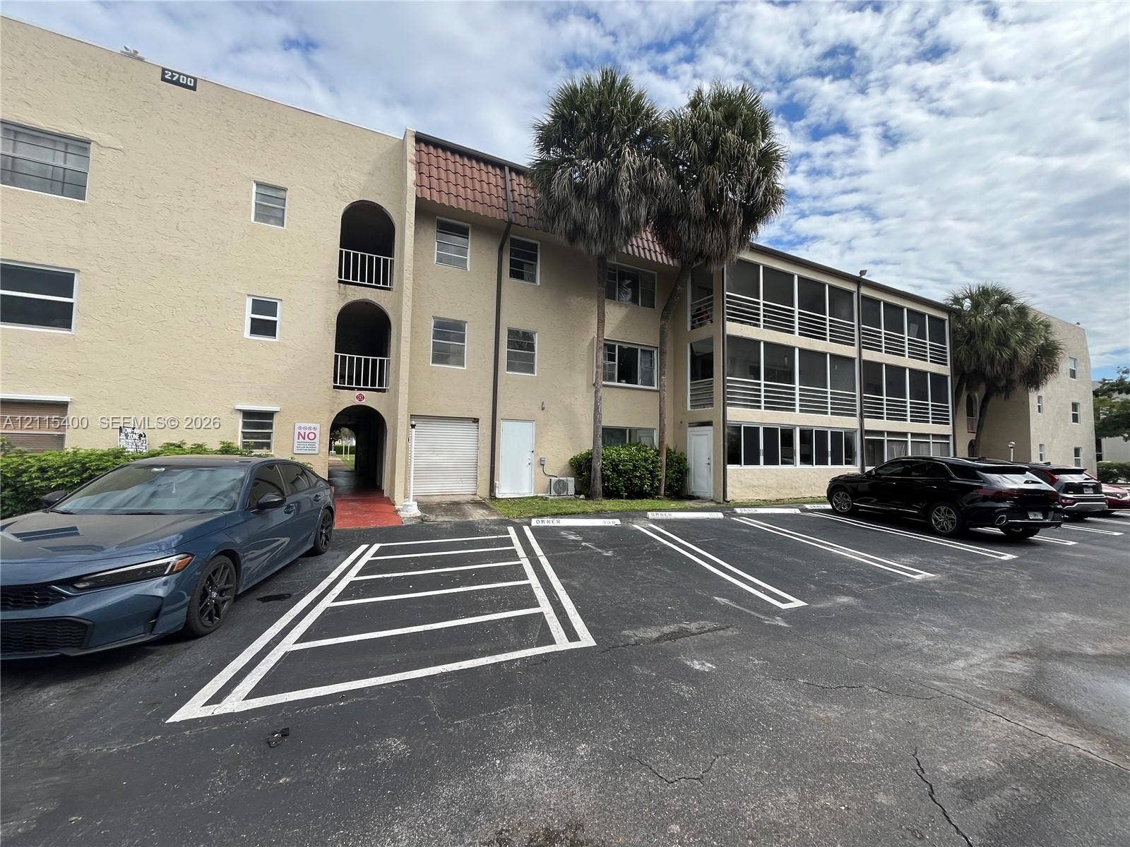 Multi-story stucco exterior featuring screened-in lanais, arched architectural detailing, and dedicated parking spaces