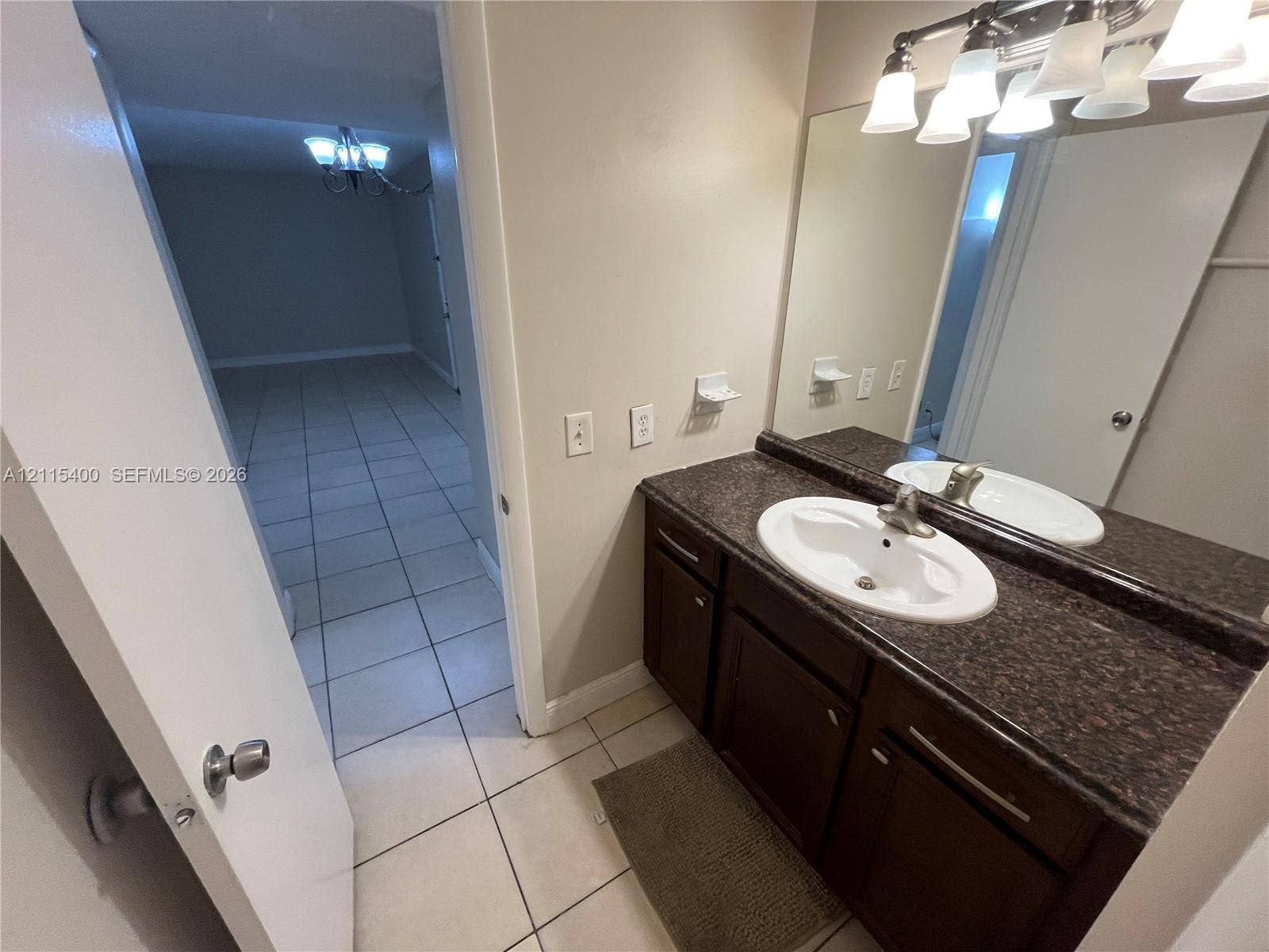 Vanity featuring a dark-finish base cabinet, solid-surface countertop, integrated oval sink, and multi-bulb light fixture