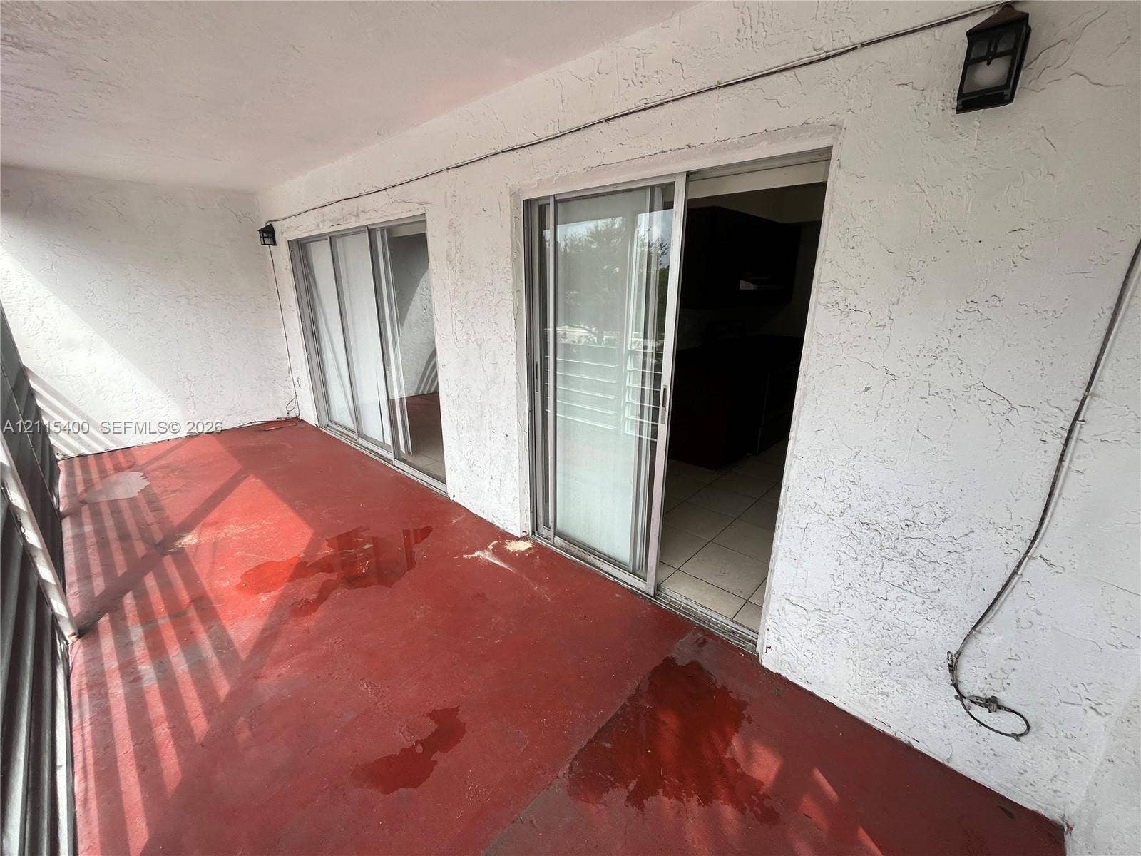 Covered balcony featuring textured stucco wall finishes, two sets of glass sliding doors, and wall-mounted exterior lighting