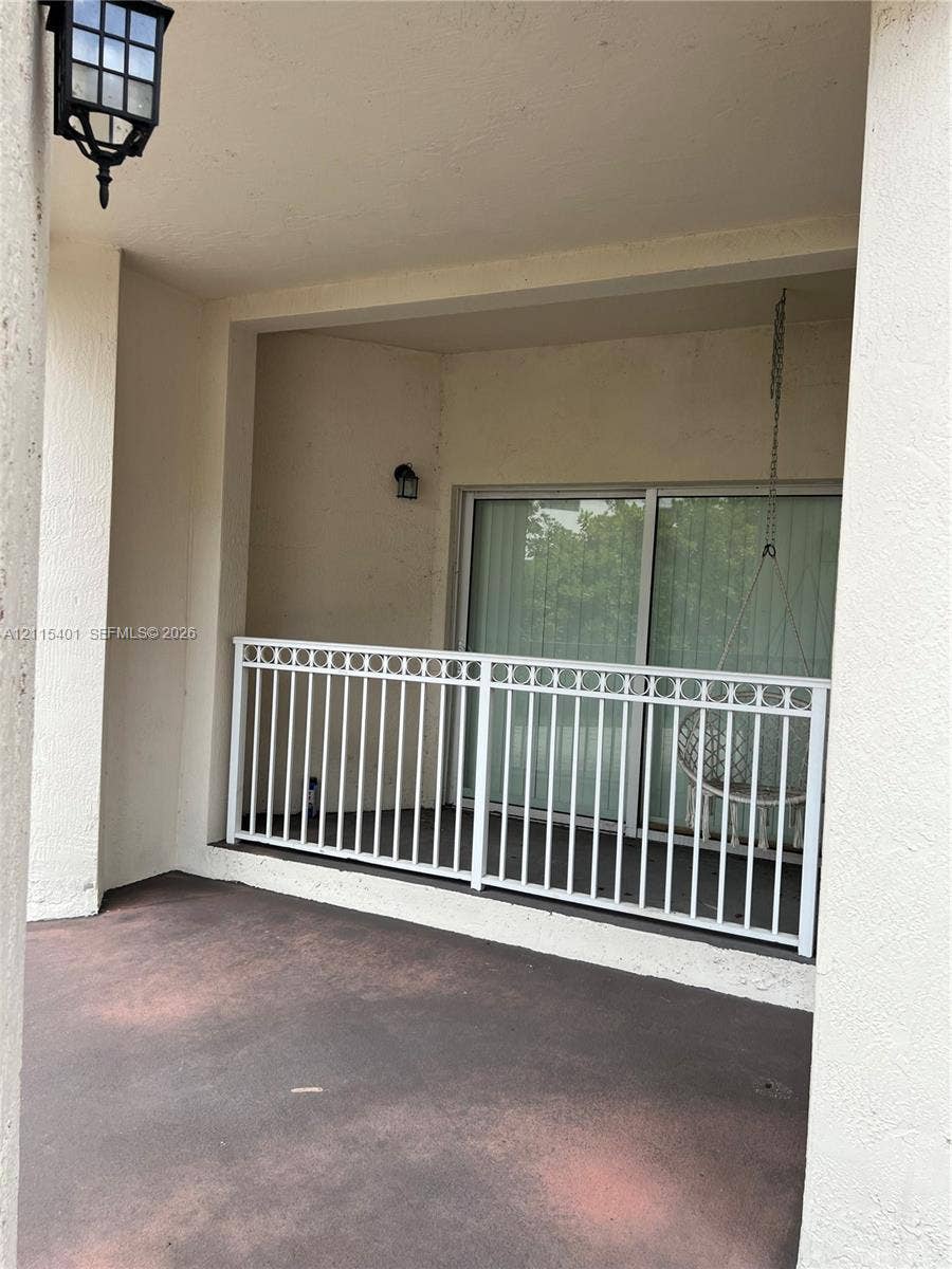 11503 NW 89th Street, #104, Doral, Doral, FL 33178 Covered balcony featuring concrete flooring, white metal railing with decorative top detailing, and exterior wall-mounted lantern lighting