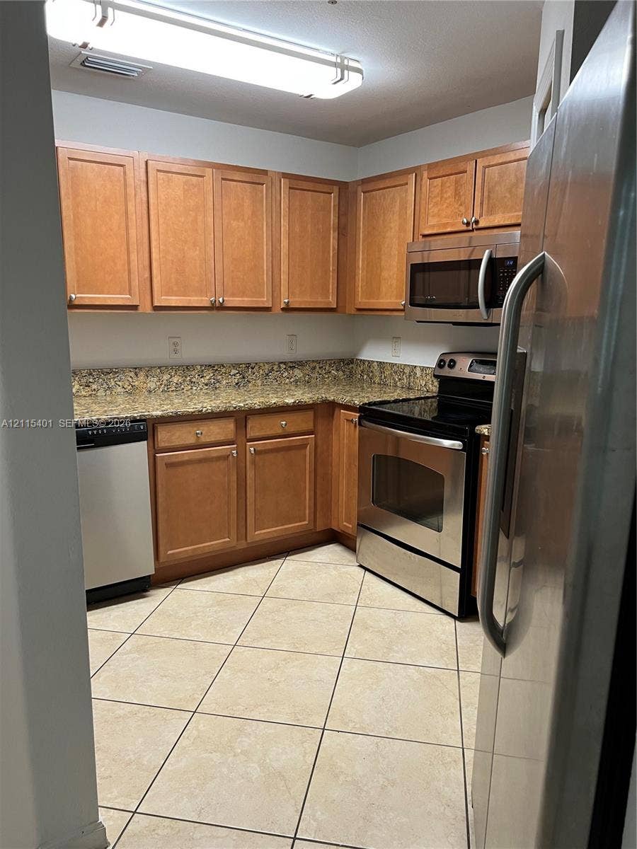 11503 NW 89th Street, #104, Doral, Doral, FL 33178 Kitchen featuring warm-tone wood cabinetry, stone countertops, stainless steel appliances, and tile flooring