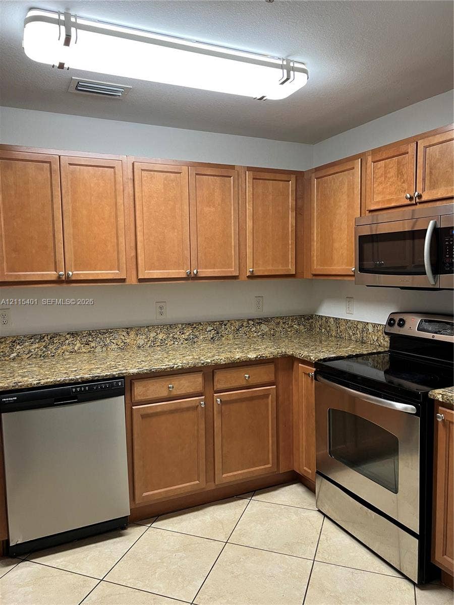 11503 NW 89th Street, #104, Doral, Doral, FL 33178 Kitchen featuring wood cabinetry, stone-surface countertops, stainless steel appliances, and tiled flooring