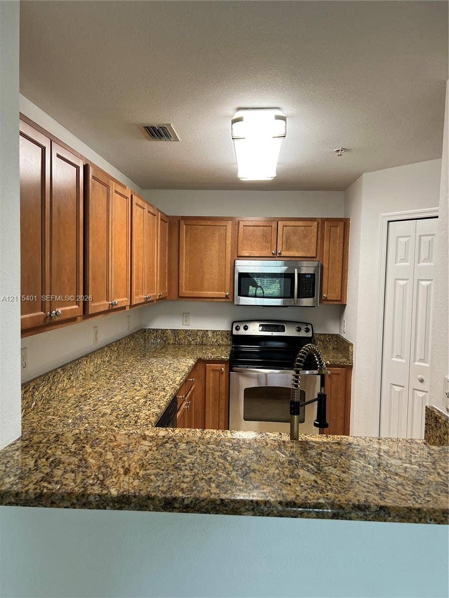 11503 NW 89th Street, #104, Doral, Doral, FL 33178 Kitchen featuring wood cabinetry, stone-surface countertops, stainless steel appliances, and a gooseneck faucet